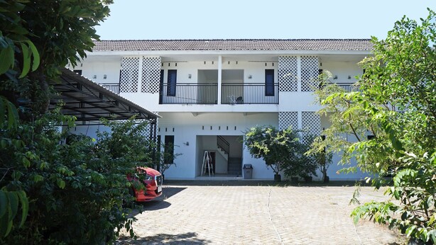 A two-story building with a tiled roof, a balcony with a railing, and a paved courtyard. - Hotel O Kost Putih Syariah (Blitar)