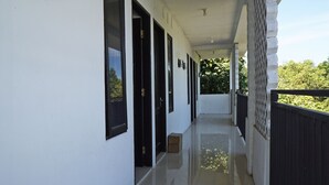 A corridor with white walls, black-framed windows, and a tiled floor leading to a balcony with a black railing. - Hotel O Kost Putih Syariah (Blitar)