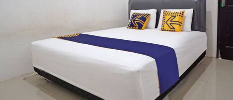A neatly made bed with a white mattress, blue bedspread, and two decorative pillows with geometric patterns.