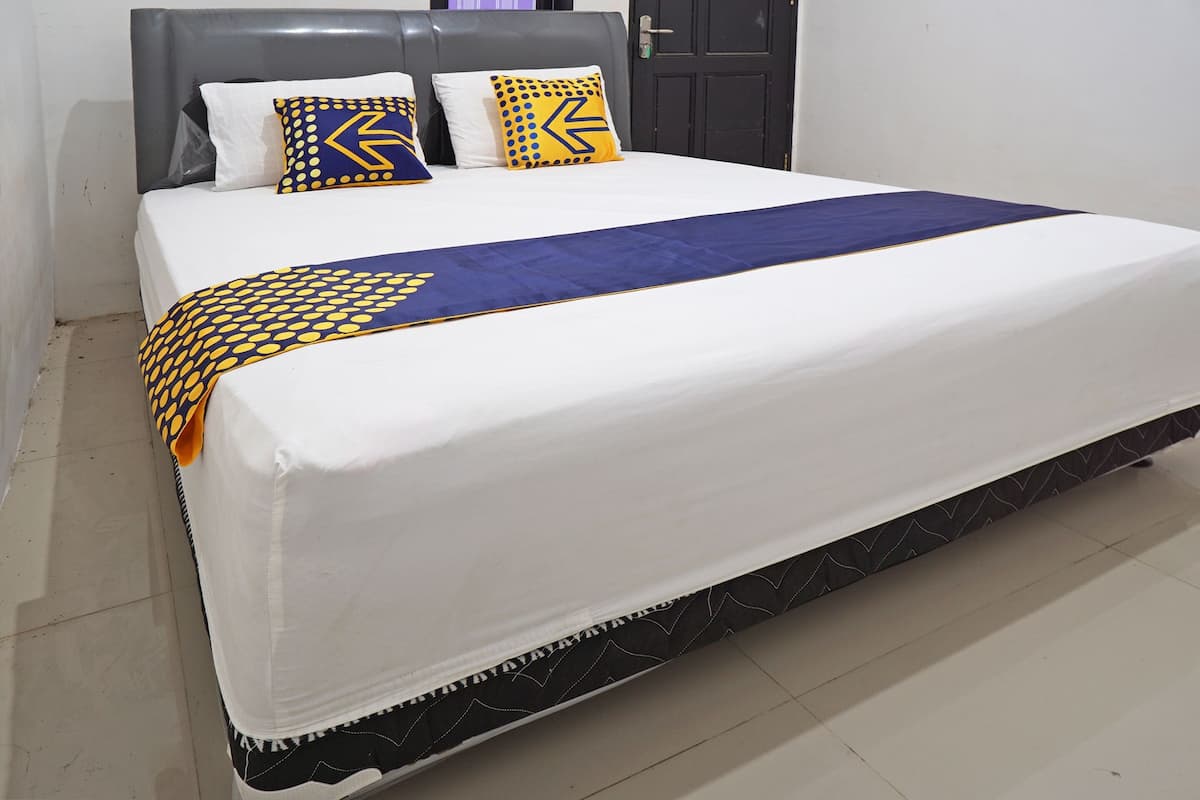 A bed with a white mattress, a grey headboard, and two pillows with a yellow and blue pattern.