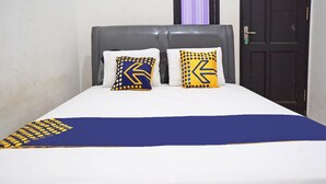 A bed with a white mattress, two pillows with a geometric pattern, and a blue and yellow blanket. - Hotel O Kost Putih Syariah (Blitar)