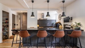 Une cuisine moderne dotée d’un îlot central, de tabourets de bar, de luminaires suspendus et d’un téléviseur encastré.