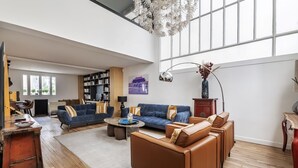 Un salon spacieux avec une grande fenêtre, un canapé bleu, un canapé marron, une table basse et une bibliothèque.