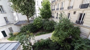 Une cour intérieure agrémentée d’une végétation luxuriante, un étroit sentier et des bâtiments dotés de balcons et de fenêtres.