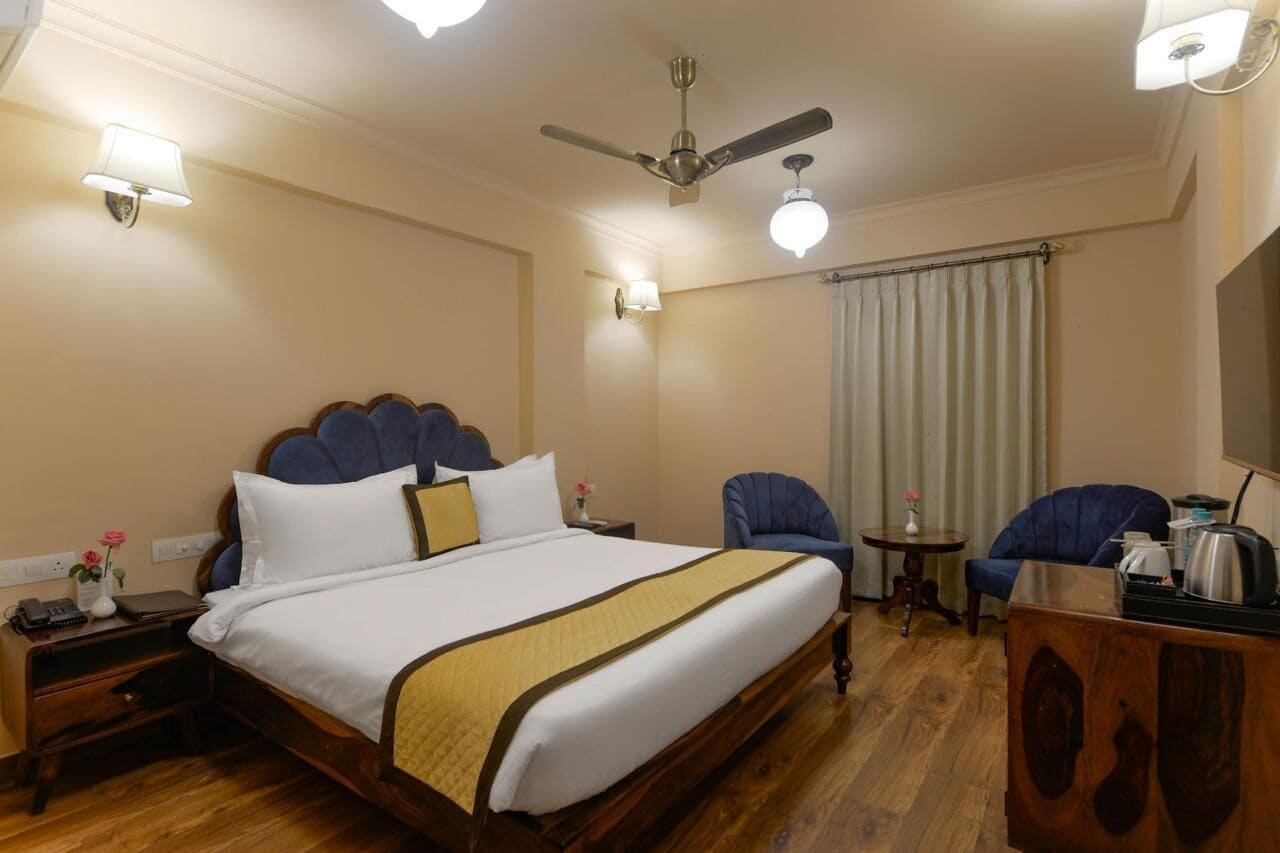 A hotel room with a large bed, a ceiling fan, a desk with a chair, and a window with curtains.