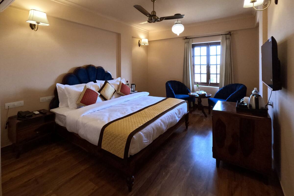 Quarto de hotel com uma cama grande, escrivaninha, cadeira, ventilador de teto e televisão.