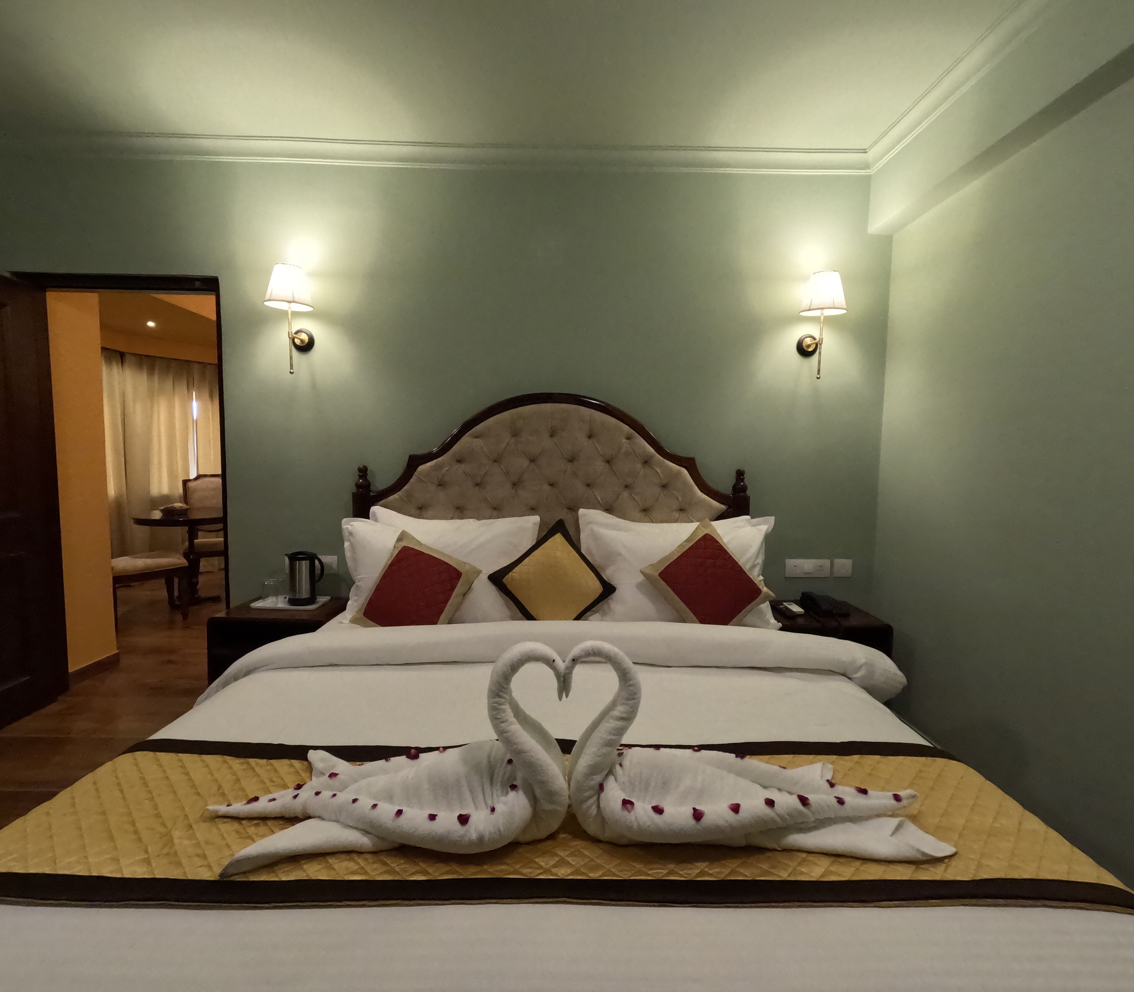 Una camera d'albergo con un letto grande, due lampade ai comodini, una testiera in legno e un decoro a forma di cigno realizzato con gli asciugamani sul letto.