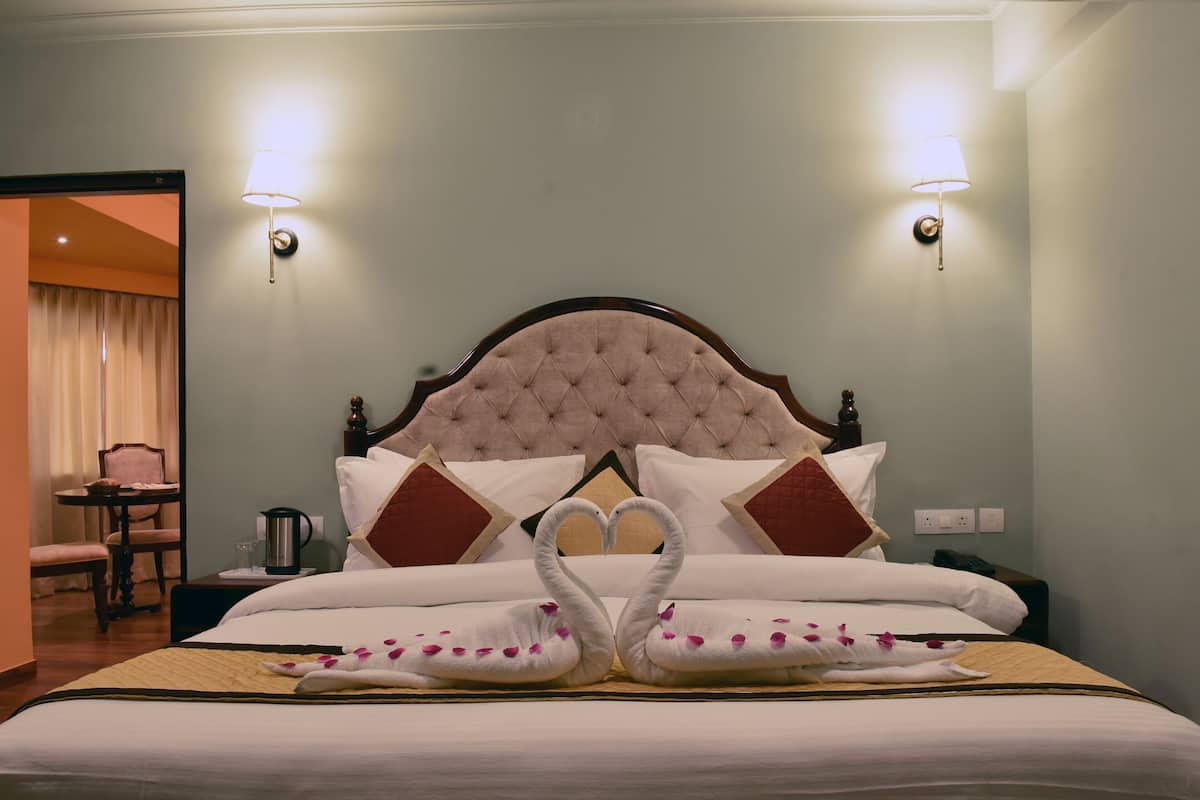 Quarto de hotel com uma cama grande, duas luminárias na parede, uma mesinha de cabeceira, uma cadeira e uma mesa.