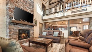 Un vaste espace de vie doté d’une cheminée, de canapés en cuir et d’un balcon avec une balustrade en bois.
