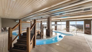 Un espace piscine doté d’un escalier en bois, offrant une vue sur l’extérieur, et agrémenté d’un panneau indiquant la présence d’un sauveteur.