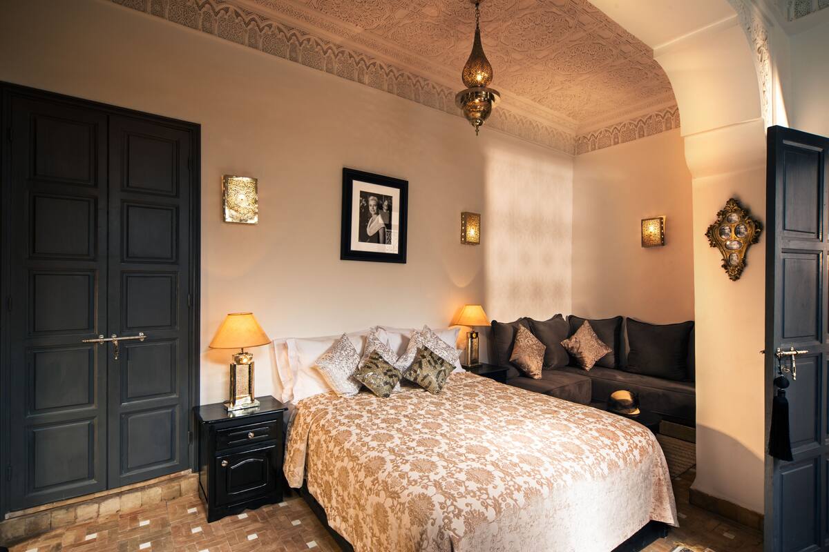 A bedroom with a large bed, two bedside tables, a wardrobe, and a chandelier.