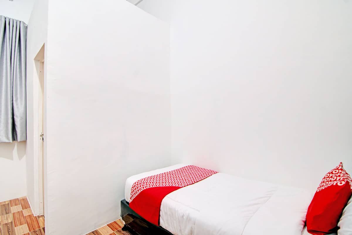 Een kleine kamer met een enkel bed, een witte muur en een houten vloer.