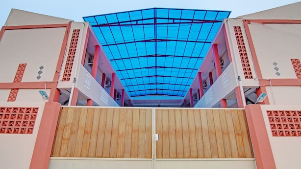 A building with a large wooden gate, a blue roof, and pink and beige walls. - OYO 92946 Dekna Homestay Syariah (Pekanbaru)