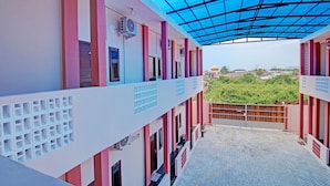 A covered outdoor area with a tiled floor, a view of greenery, and a building with pink and white walls and a blue roof. - OYO 92946 Dekna Homestay Syariah (Pekanbaru)