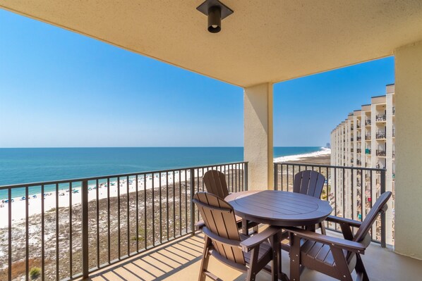 A balcony with a table and chairs, overlooking a beach and ocean. - Beachfront Getaway at Phoenix 8, 1202 (Orange Beach)