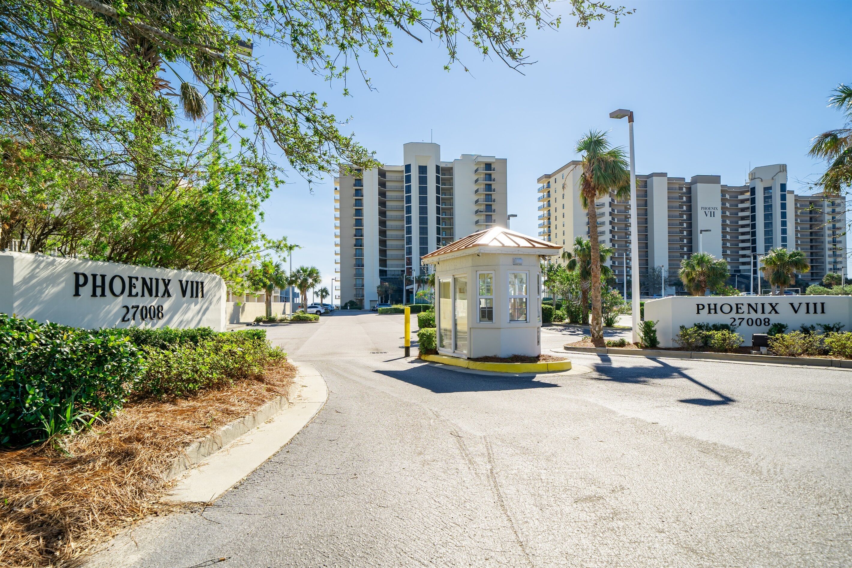 Una entrada portonada a un complejo residencial llamado Phoenix VIII, con un pequeño quiosco, edificios altos y palmeras.