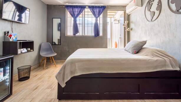 A bedroom with a bed, a chair, a TV, and a window with curtains. - Agua Azul by tuhost (Guadalupe)