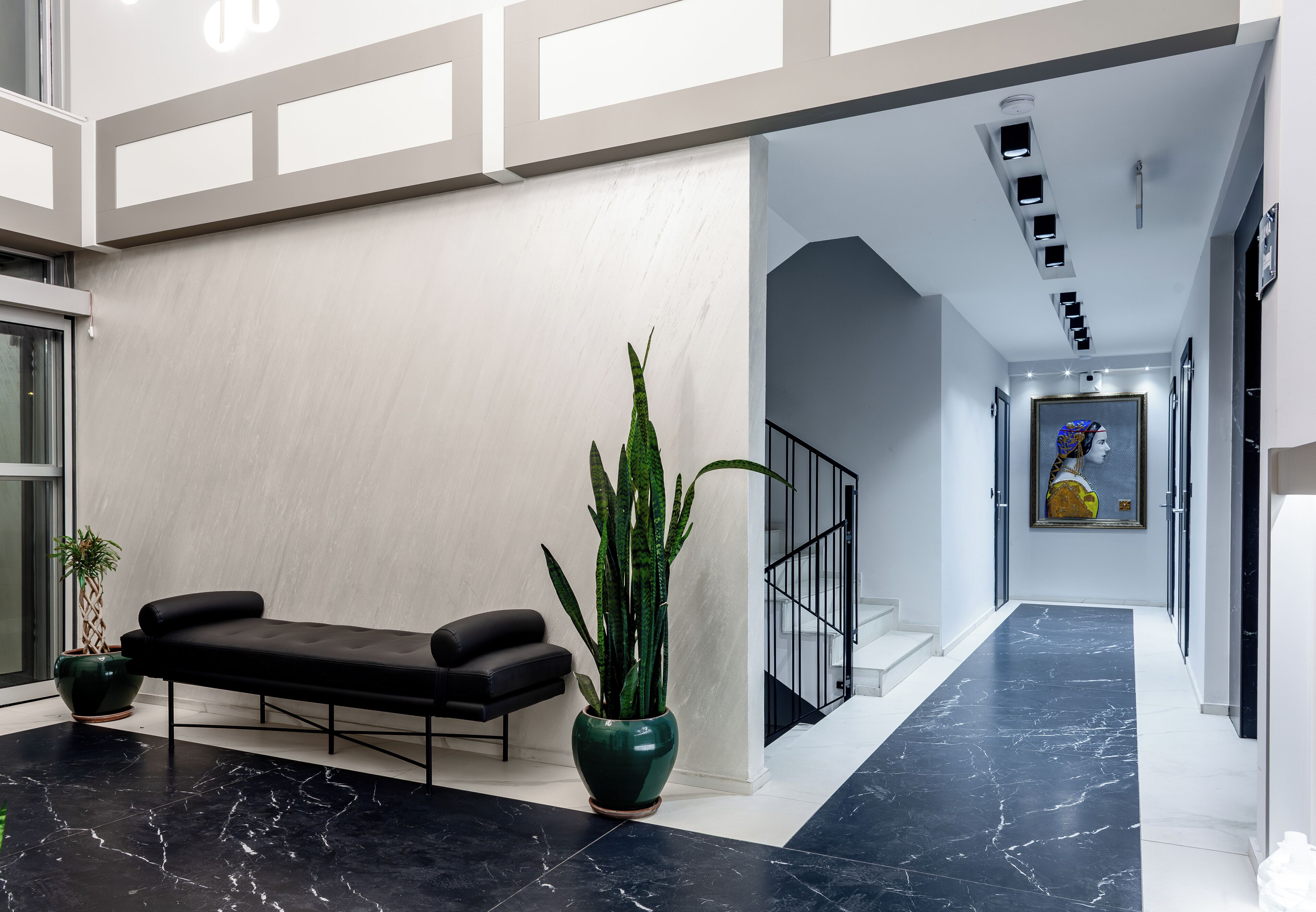 A modern lobby with a black leather bench, a large green plant, and a marble floor.