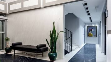 A modern lobby with a black leather bench, a large green plant, and a marble floor.