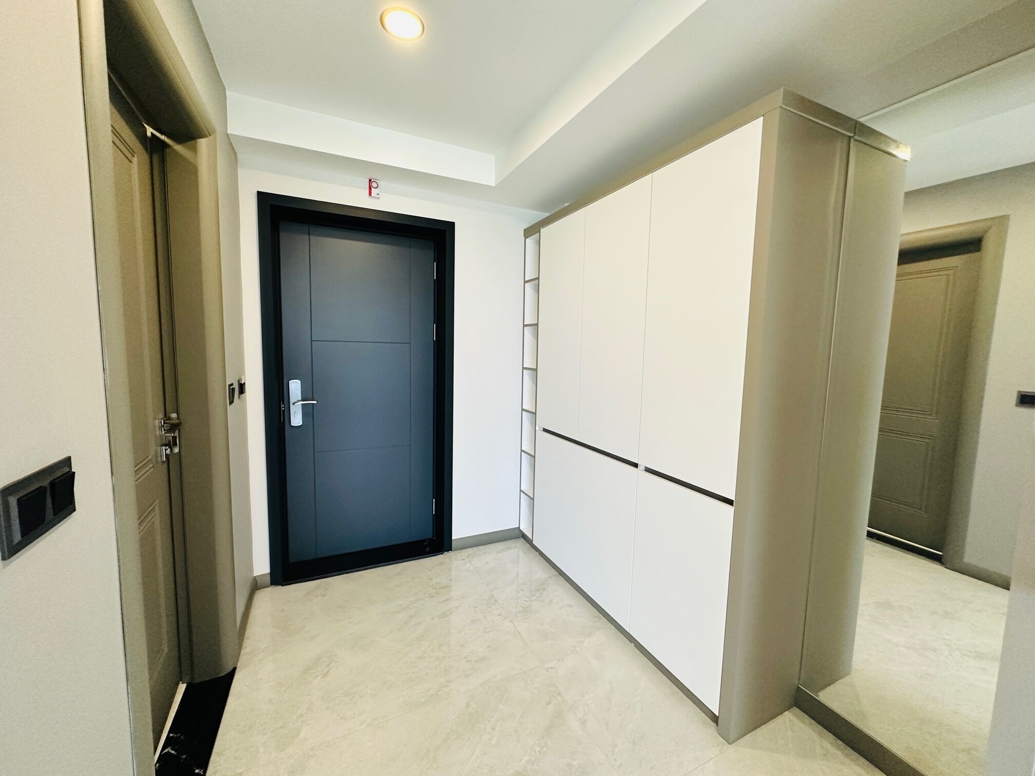 A hallway with a closed door, a light switch, and a white wardrobe.