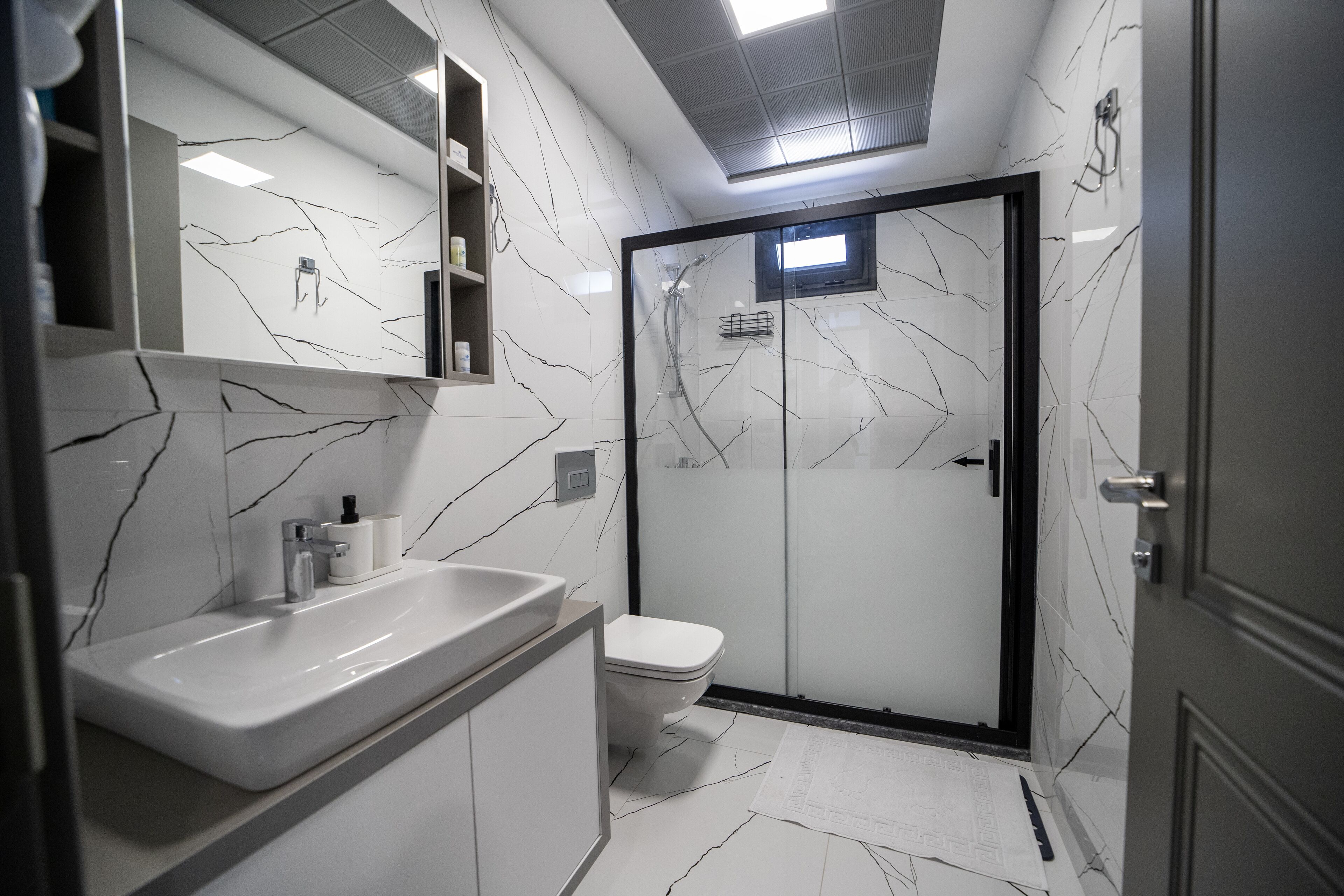 A modern bathroom with a white marble backsplash, a large sink, a toilet, and a glass-enclosed shower.