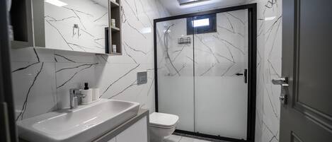 A modern bathroom with a white marble backsplash, a large sink, a toilet, and a glass-enclosed shower.