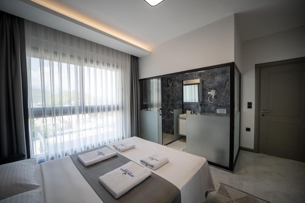 Een moderne hotelkamer met een groot bed, een badkamer met een douchecabine van glas, en uitzicht op het omliggende landschap.