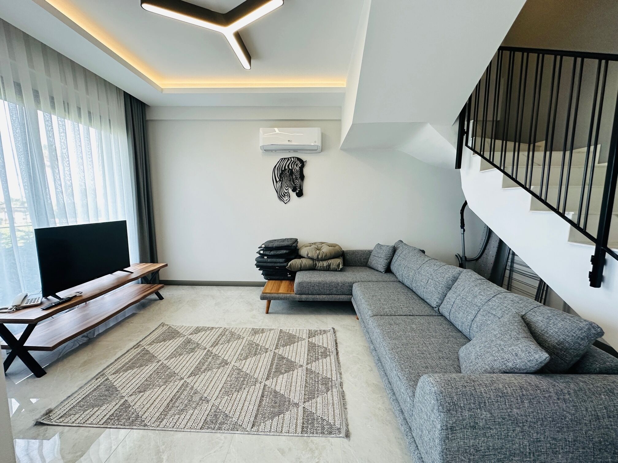 A modern living room with a sectional sofa, a flat-screen TV, a wooden coffee table, and a patterned rug.