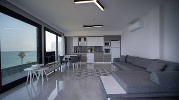 Un salon moderne avec un canapé gris, un coin repas avec une table blanche et une cuisine avec des meubles blancs.