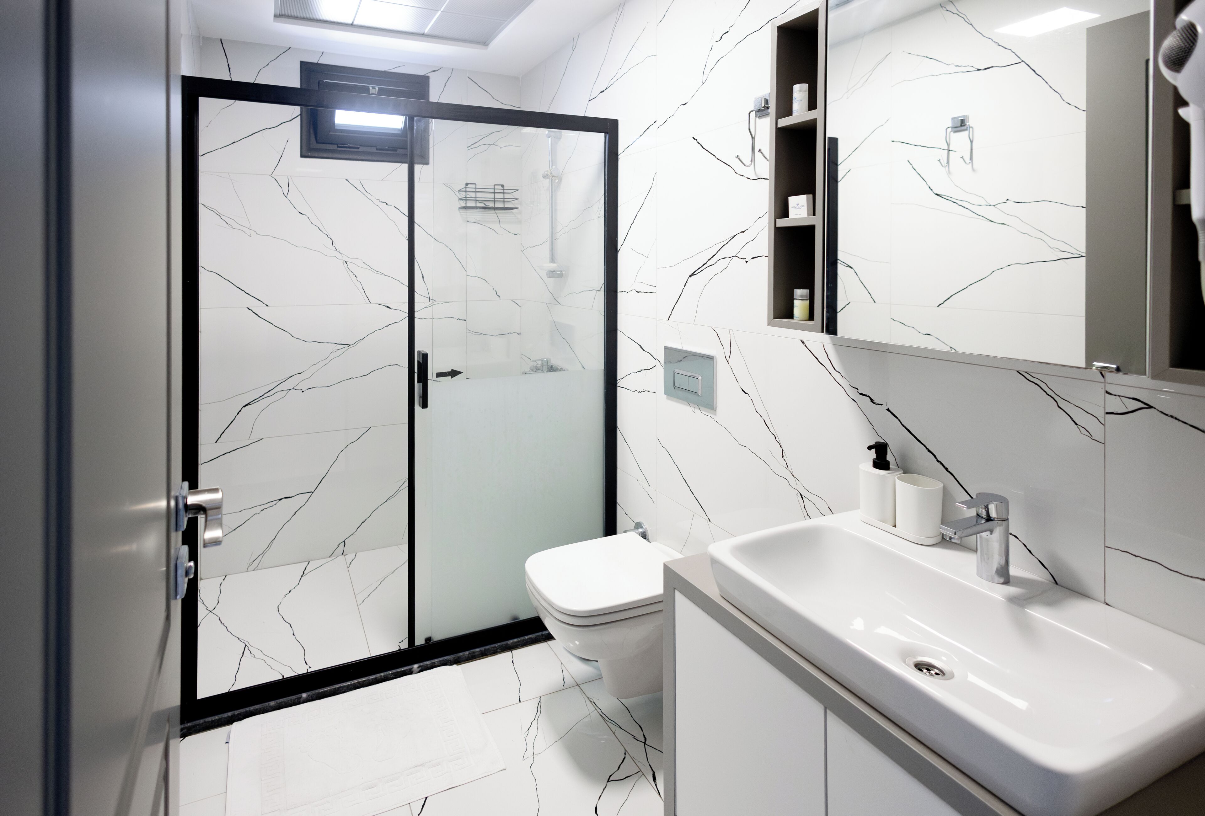 A modern bathroom with a glass-enclosed shower, a white toilet, and a sink with a mirror above it.