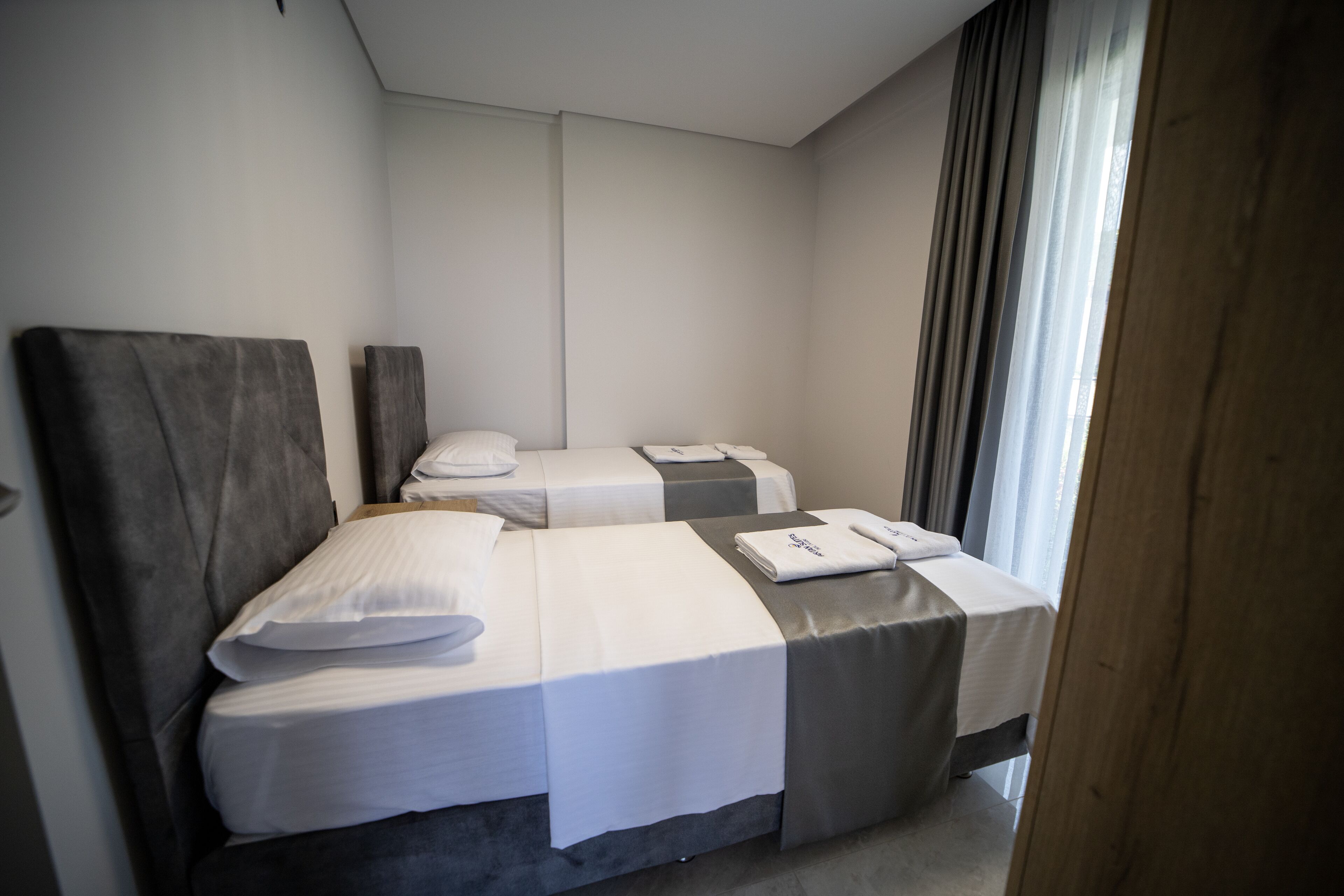 A hotel room with two beds, a large window with curtains, and a wooden door.