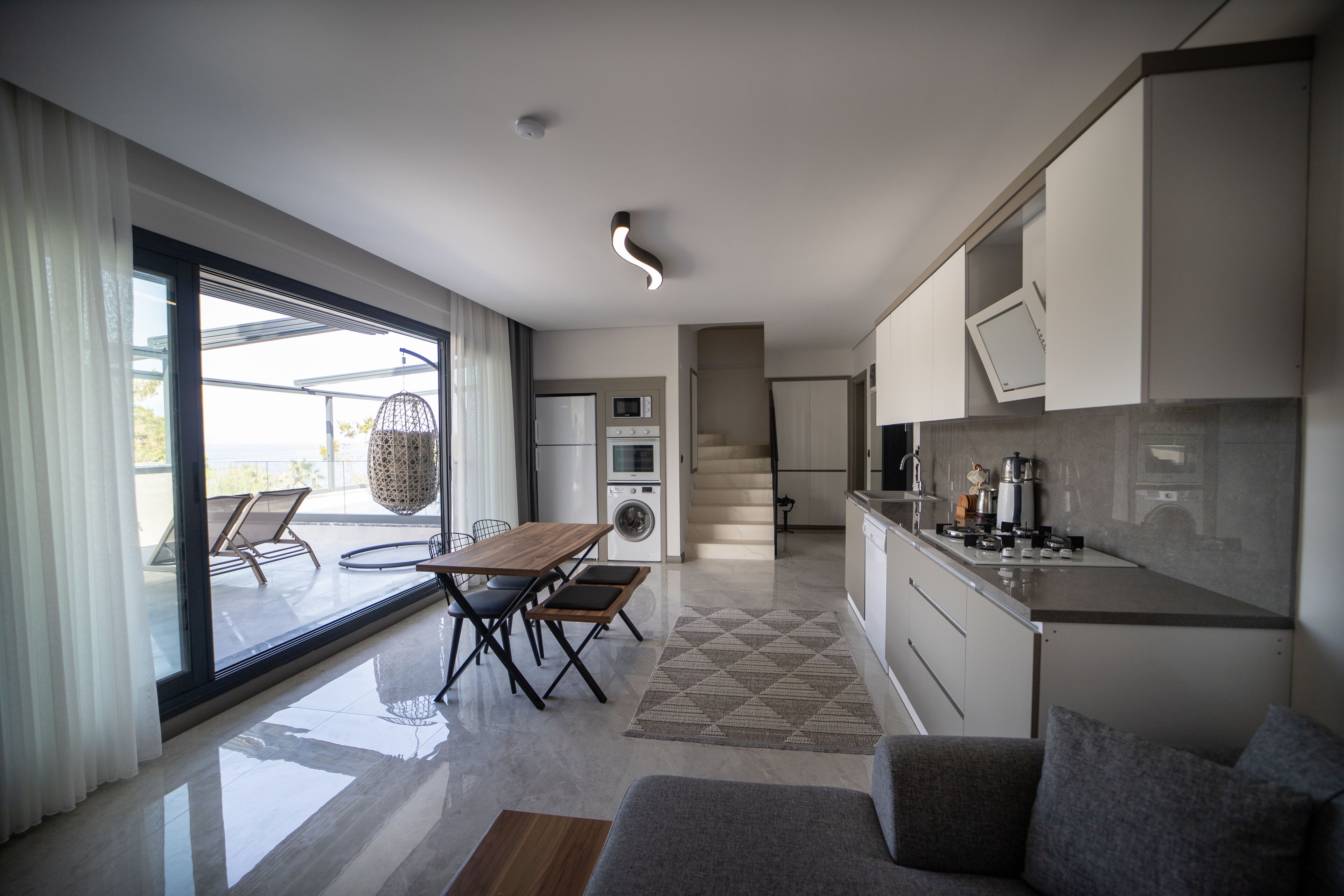 A modern kitchen with a dining area, large windows, and a view of the outdoors.