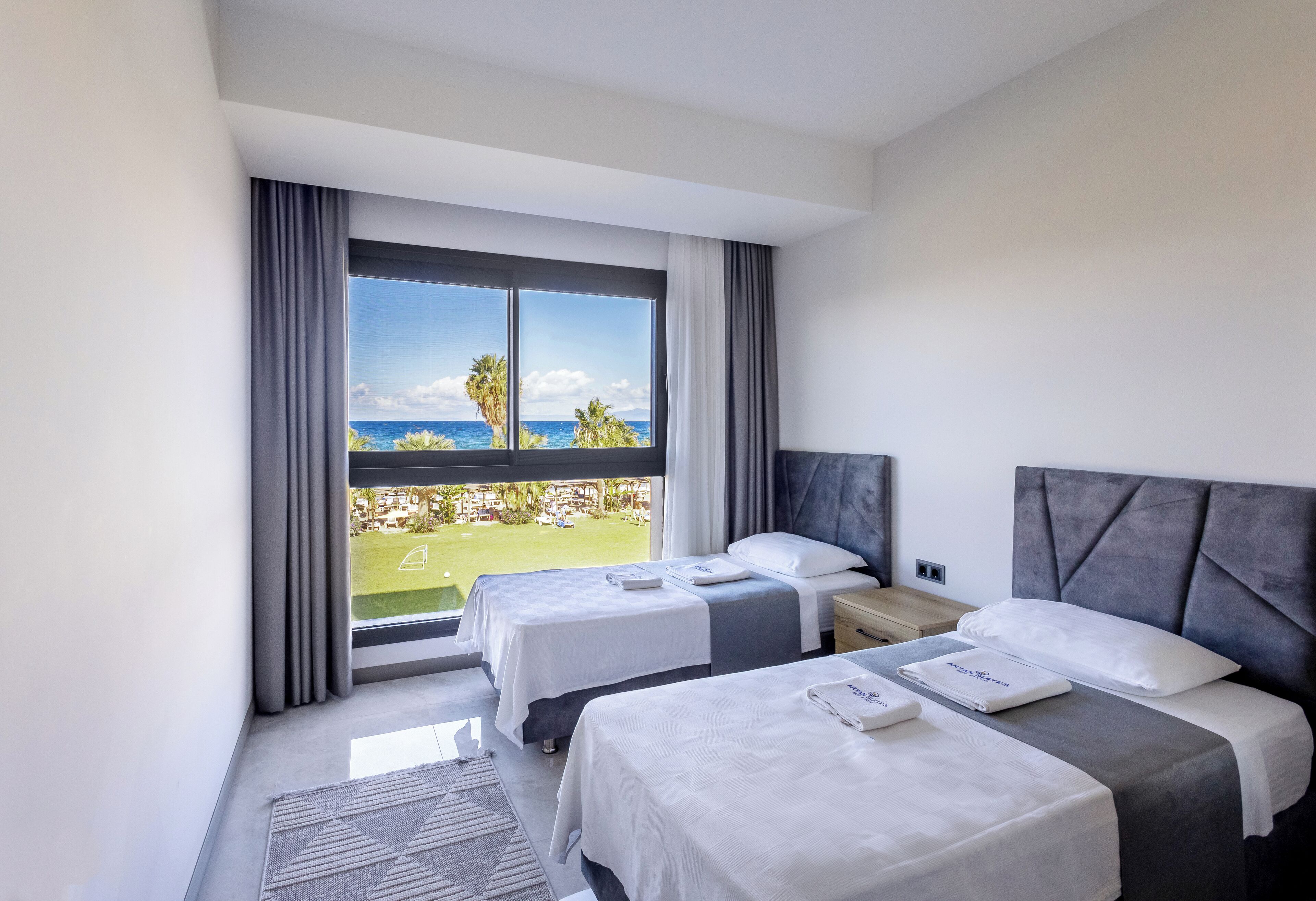 Ein Hotelzimmer mit zwei Betten, einem großen Fenster mit Blick auf das Meer und Palmen sowie einem modernen Design.