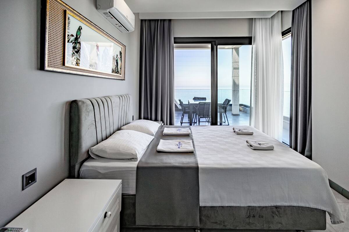 Een moderne hotelkamer met een groot bed, een nachtkastje, een klein bureau en uitzicht op het balkon en de oceaan.