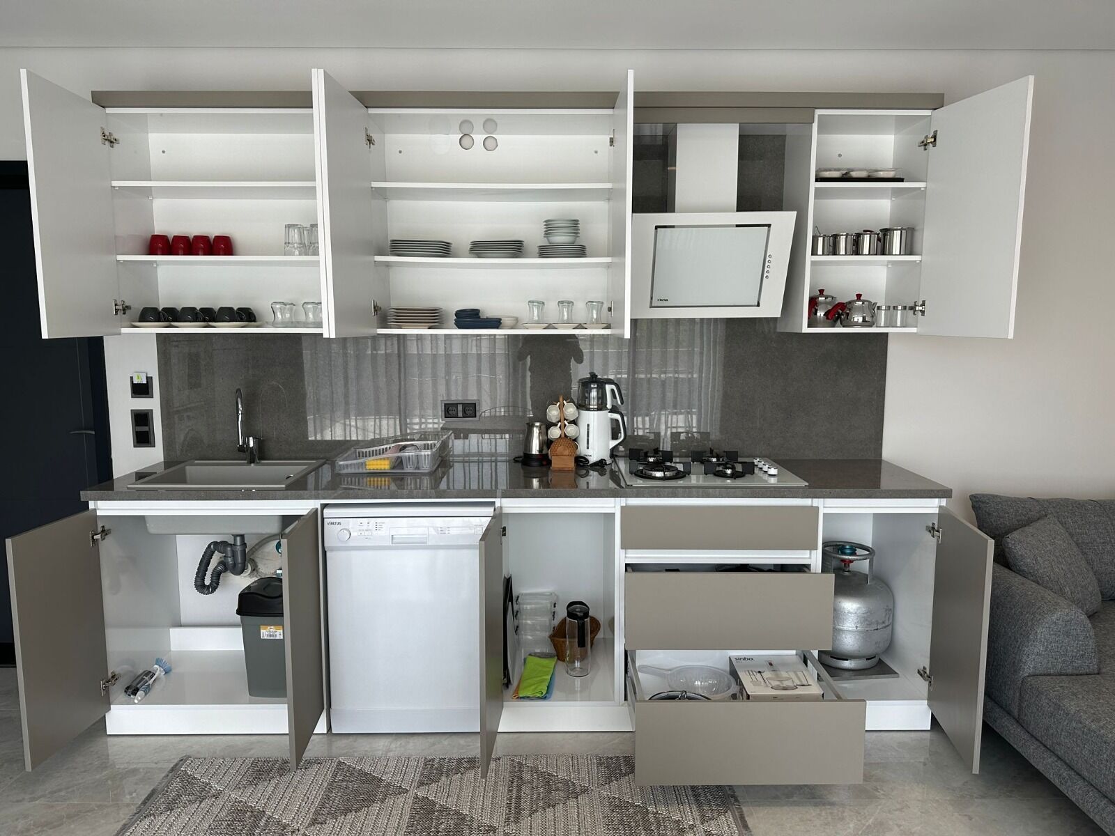 A compact kitchen with integrated appliances, open shelving, and a built-in gas stove.