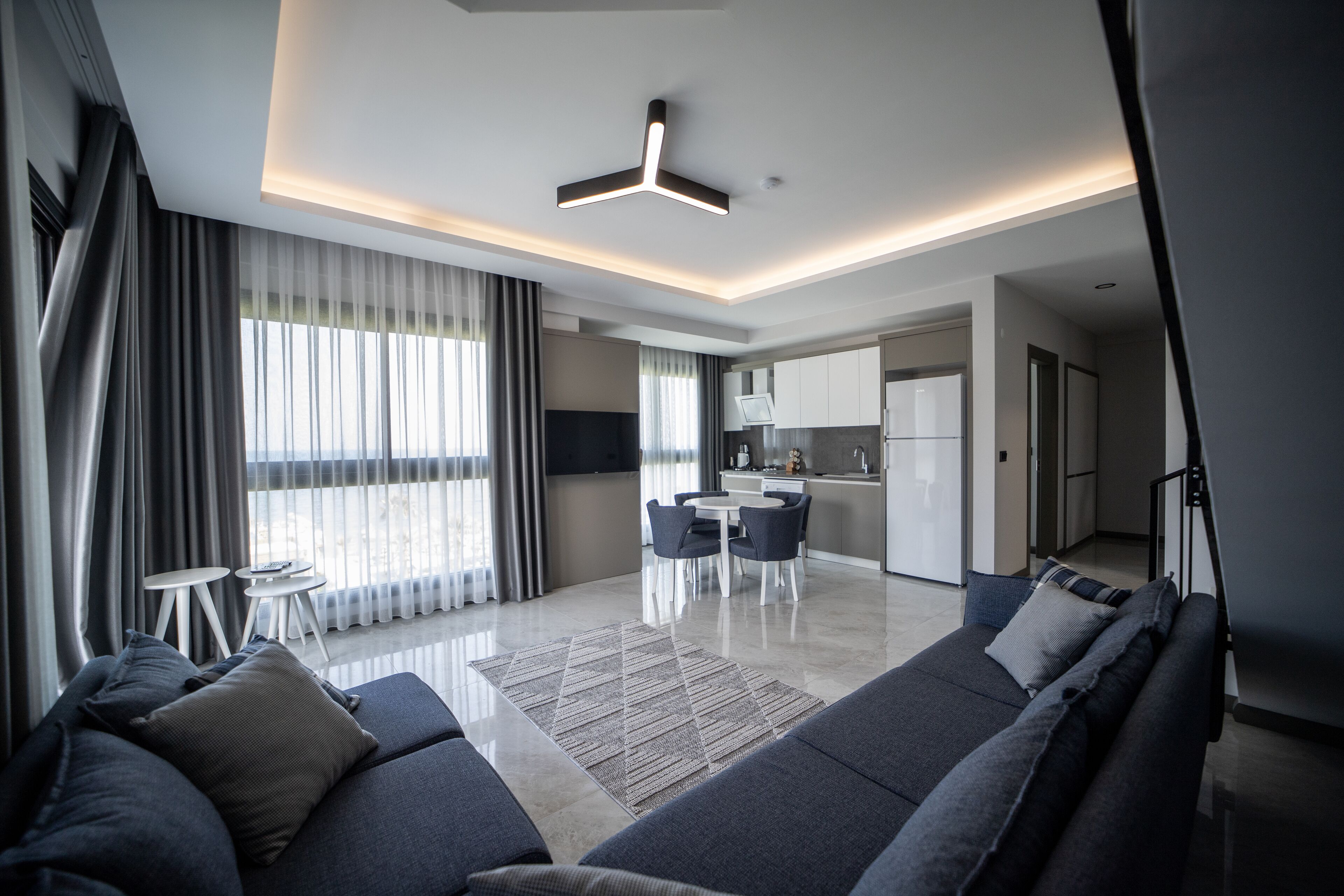 A modern living room with a sofa, a dining area with a table and chairs, and a kitchen in the background.