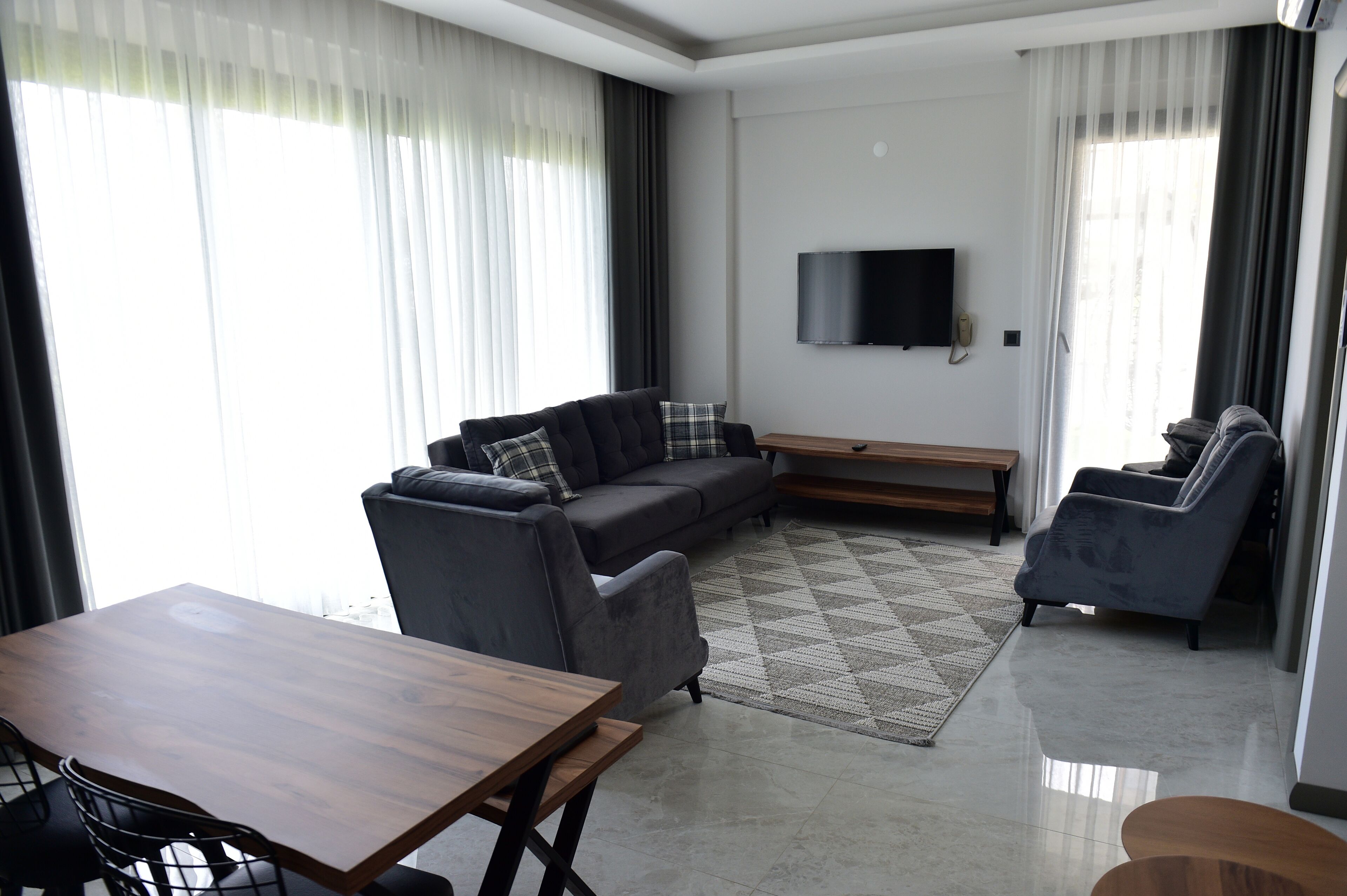 A modern living room with a sofa, armchair, and a TV mounted on the wall.