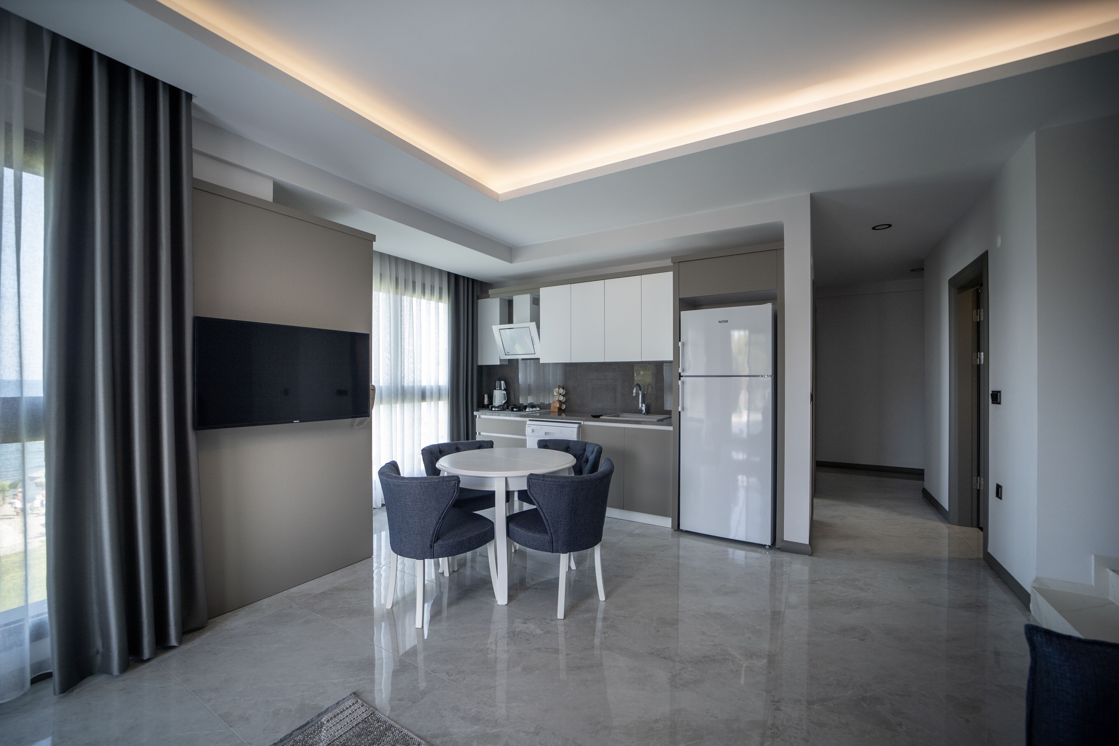 Una cocina moderna con armarios blancos, horno empotrado y refrigerador. Hay un comedor con una mesa redonda y sillas.