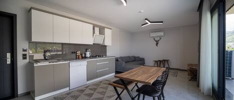 A modern kitchen with a dining area, featuring a wooden table and chairs, a grey sofa, and contemporary lighting fixtures.