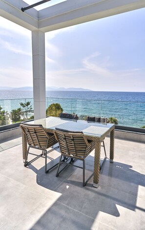 Una terraza con una mesa de vidrio y sillas de mimbre, con vistas al mar.