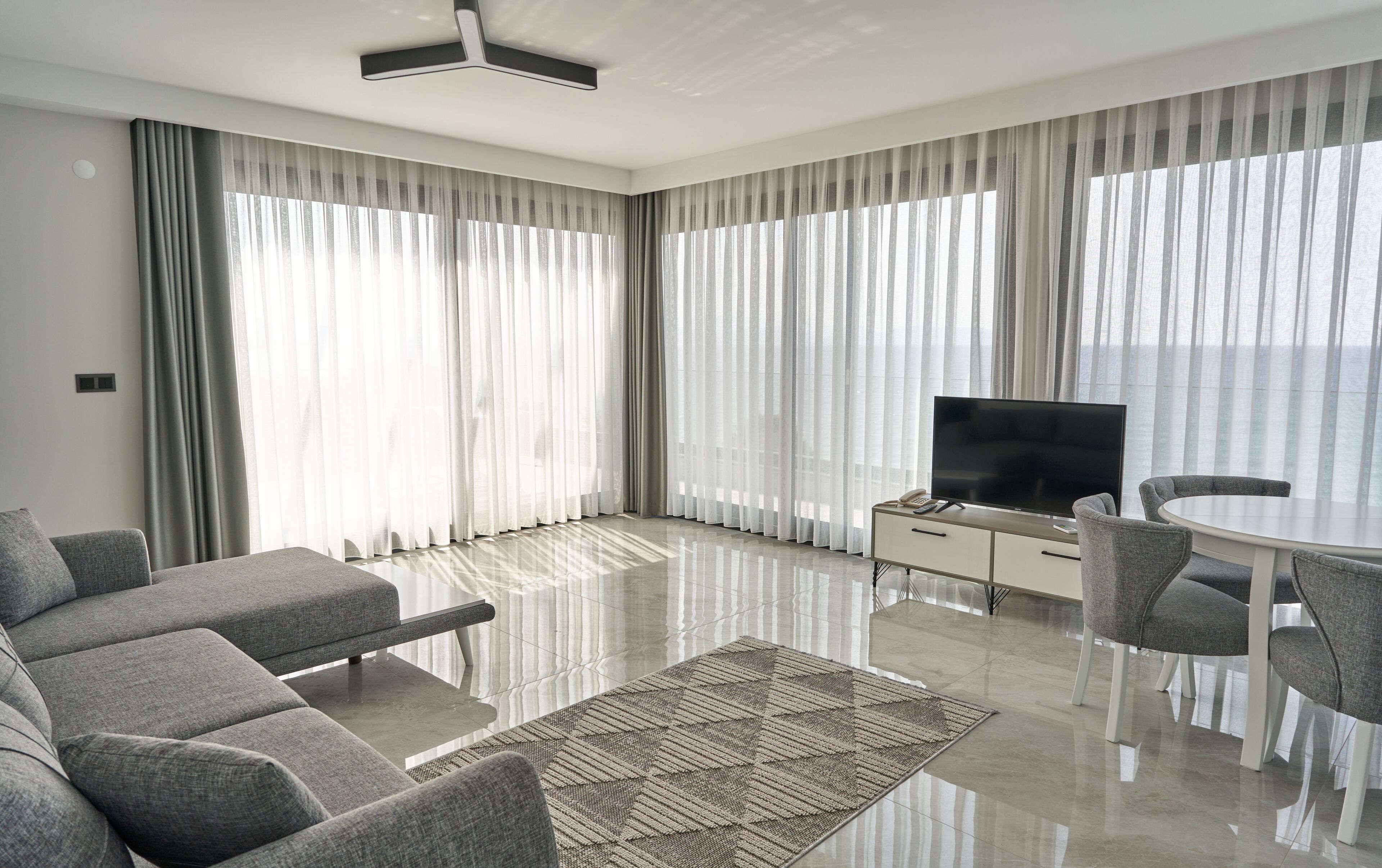 A modern living room with a flat-screen TV, grey sofa, dining table, and chairs.