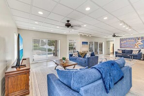 A spacious living room with a large blue sofa, a wooden coffee table, and a TV on a stand. - Luxury 6BR Retreat with Beach Access (Sarasota)