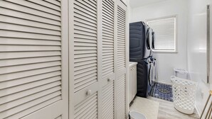 Un baño con taquillas blancas, un electrodoméstico negro y un cesto de ropa blanca.