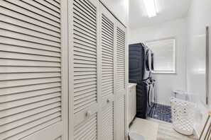 Une salle de bain avec des casiers blancs, un appareil électroménager noir et un panier à linge blanc.