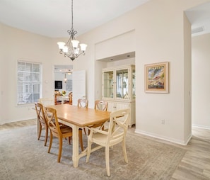 A dining room with a wooden table and chairs, a chandelier, and a cabinet with glass doors. - Luxury 6BR Retreat with Beach Access (Sarasota)