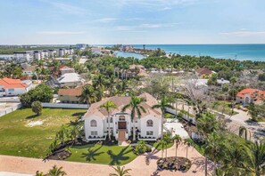 A large, white, two-story house with a central entrance, surrounded by a well-maintained lawn and palm trees. - Luxury 6BR Retreat with Beach Access (Sarasota)