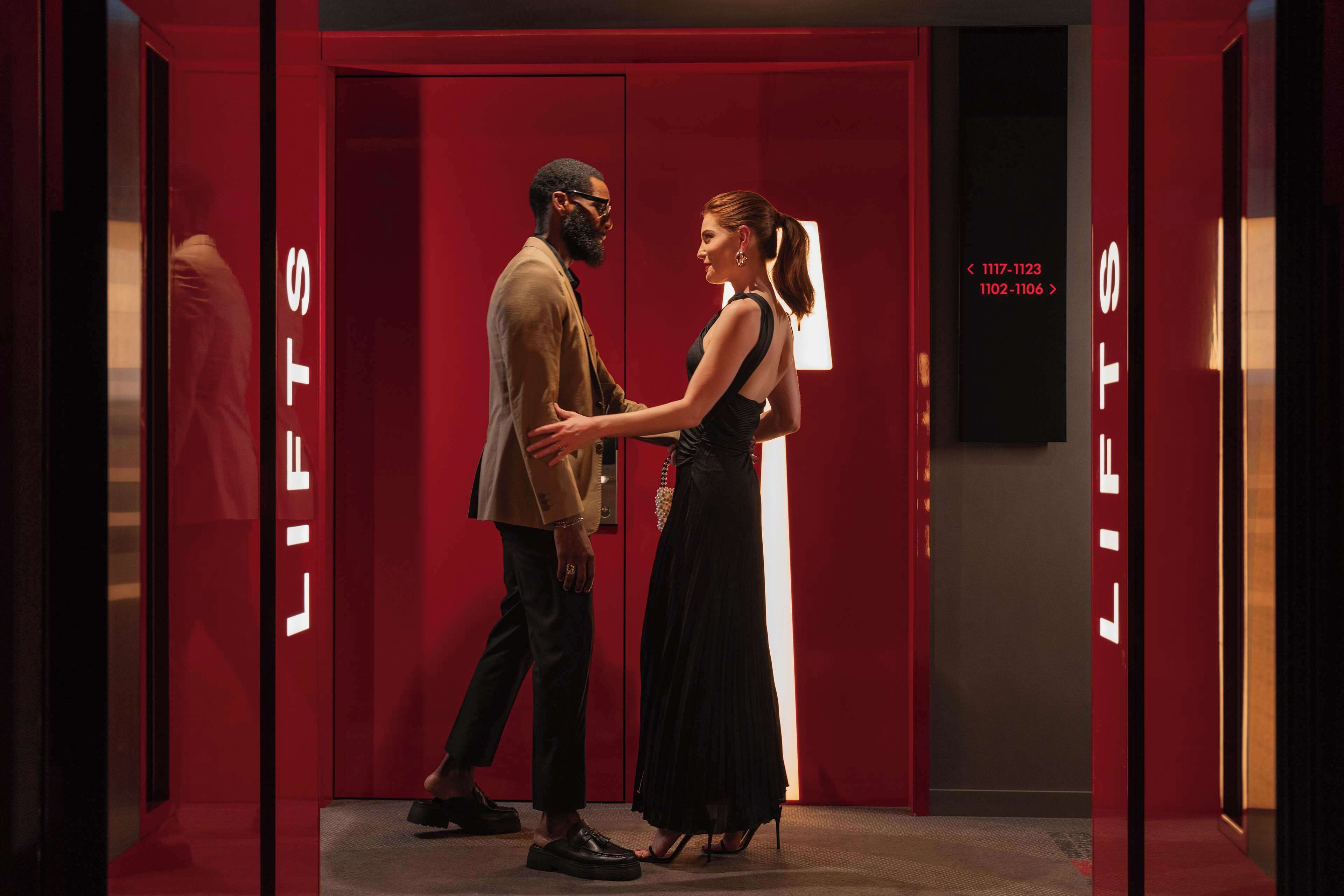 A couple in a red elevator with 'LIFTS' signage.