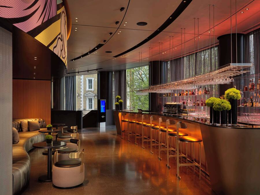 A modern bar area with a curved counter, bar stools, and a seating area with a sofa and round tables.