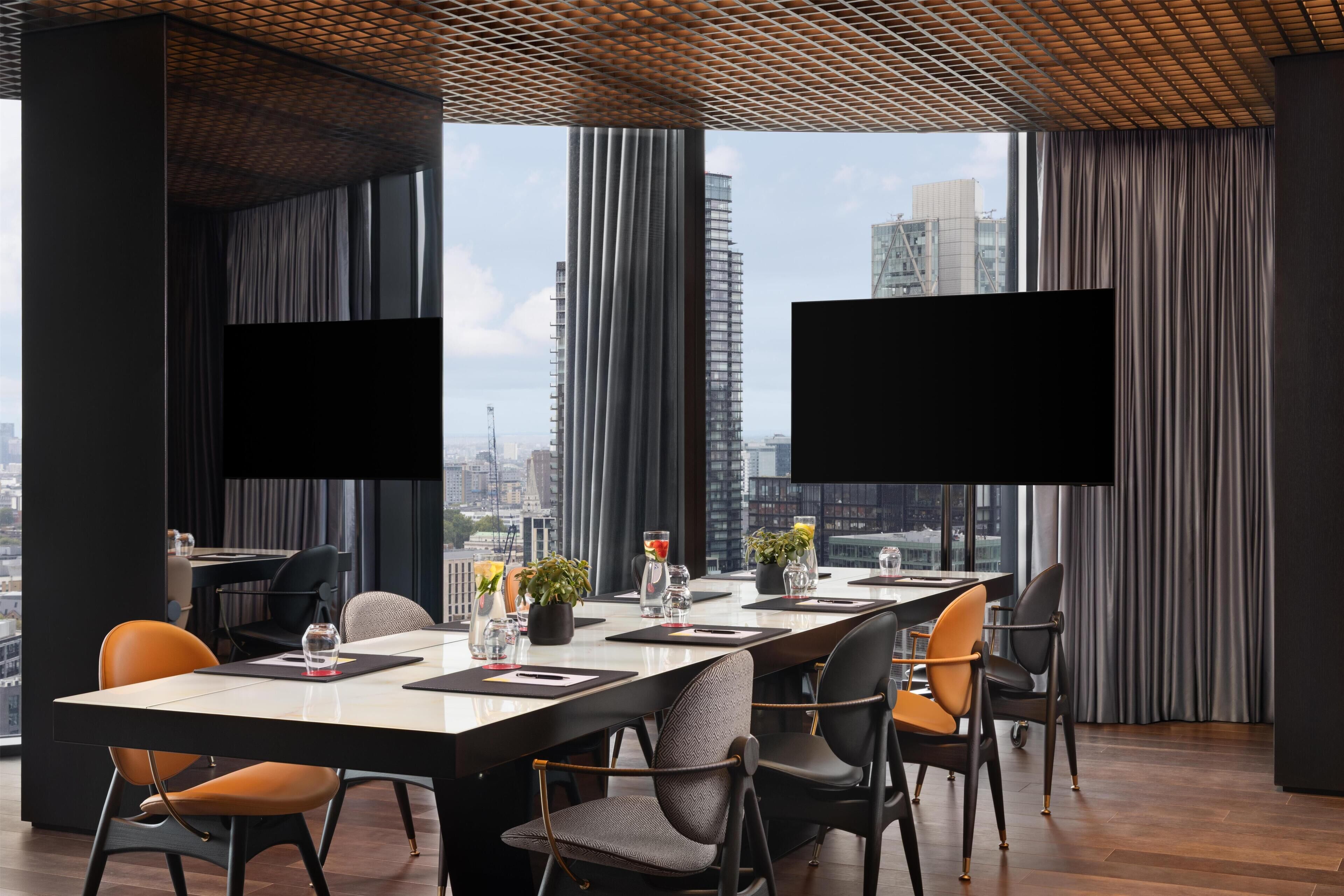 A modern conference room with a long table, chairs, and two large screens.