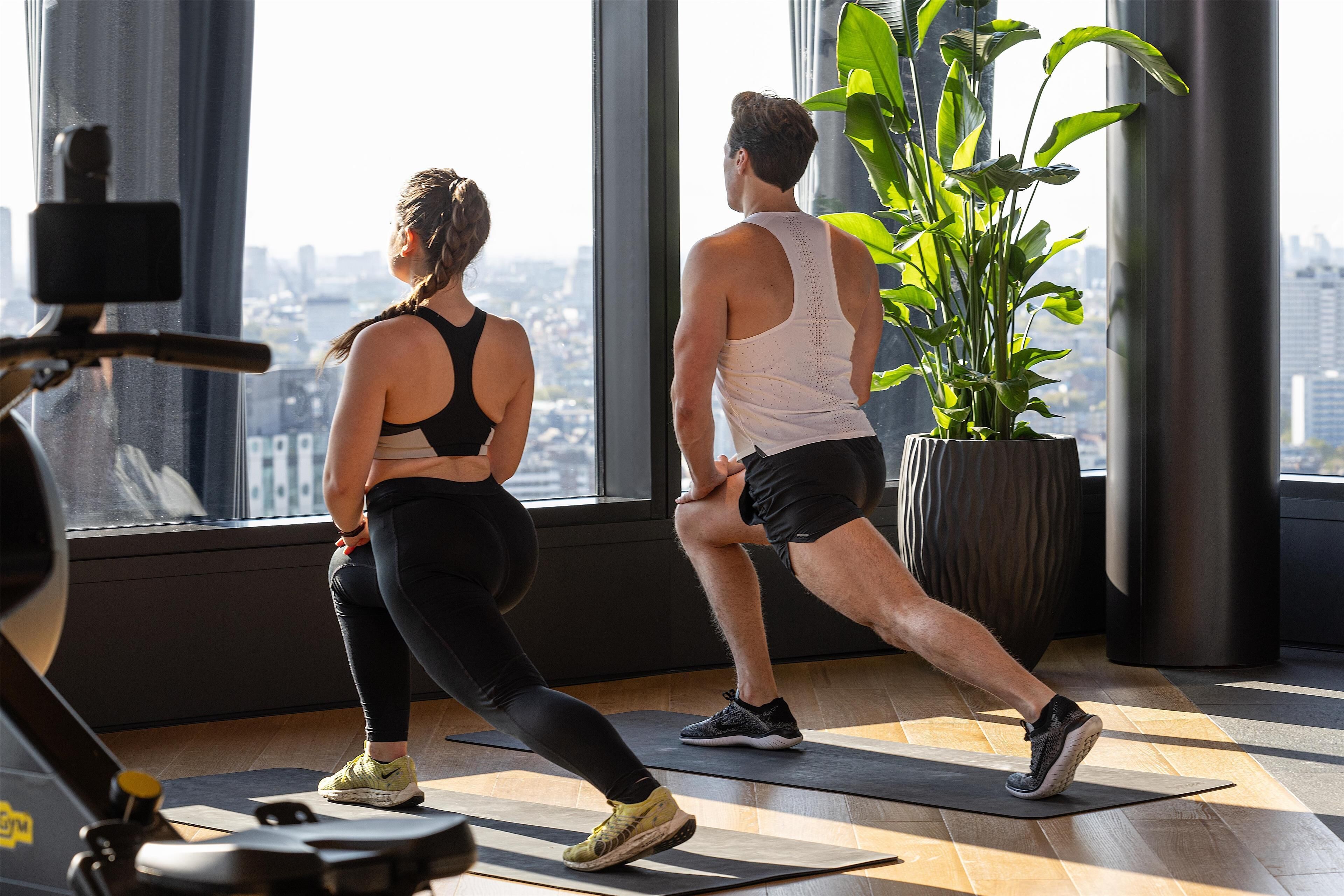 Et fitnesscenter med store vinduer, træningsudstyr og en potteplante.